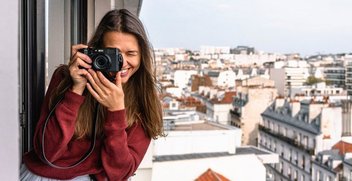 Eine Frau steht auf einem Balkon und macht ein Foto über den Dächern von Paris.