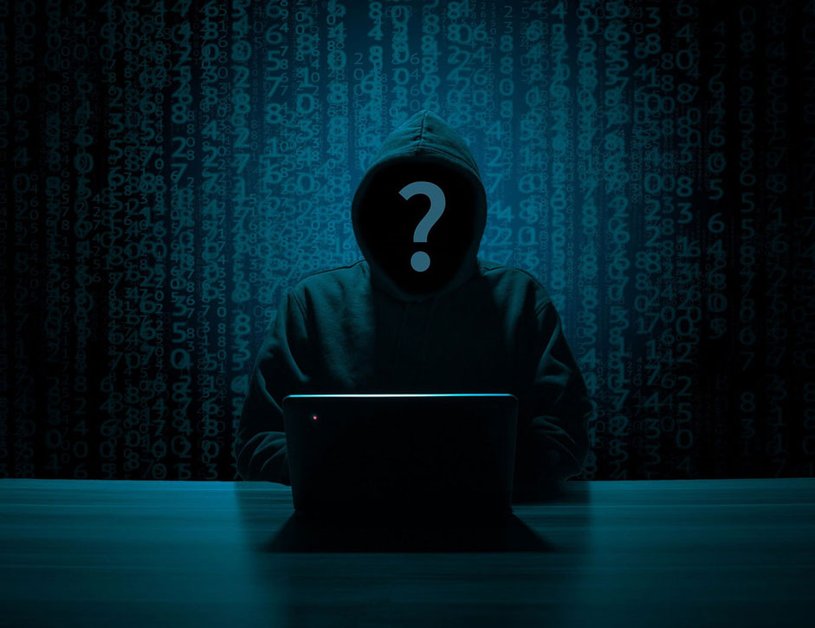 A hacker sits in a dark room in front of his laptop.