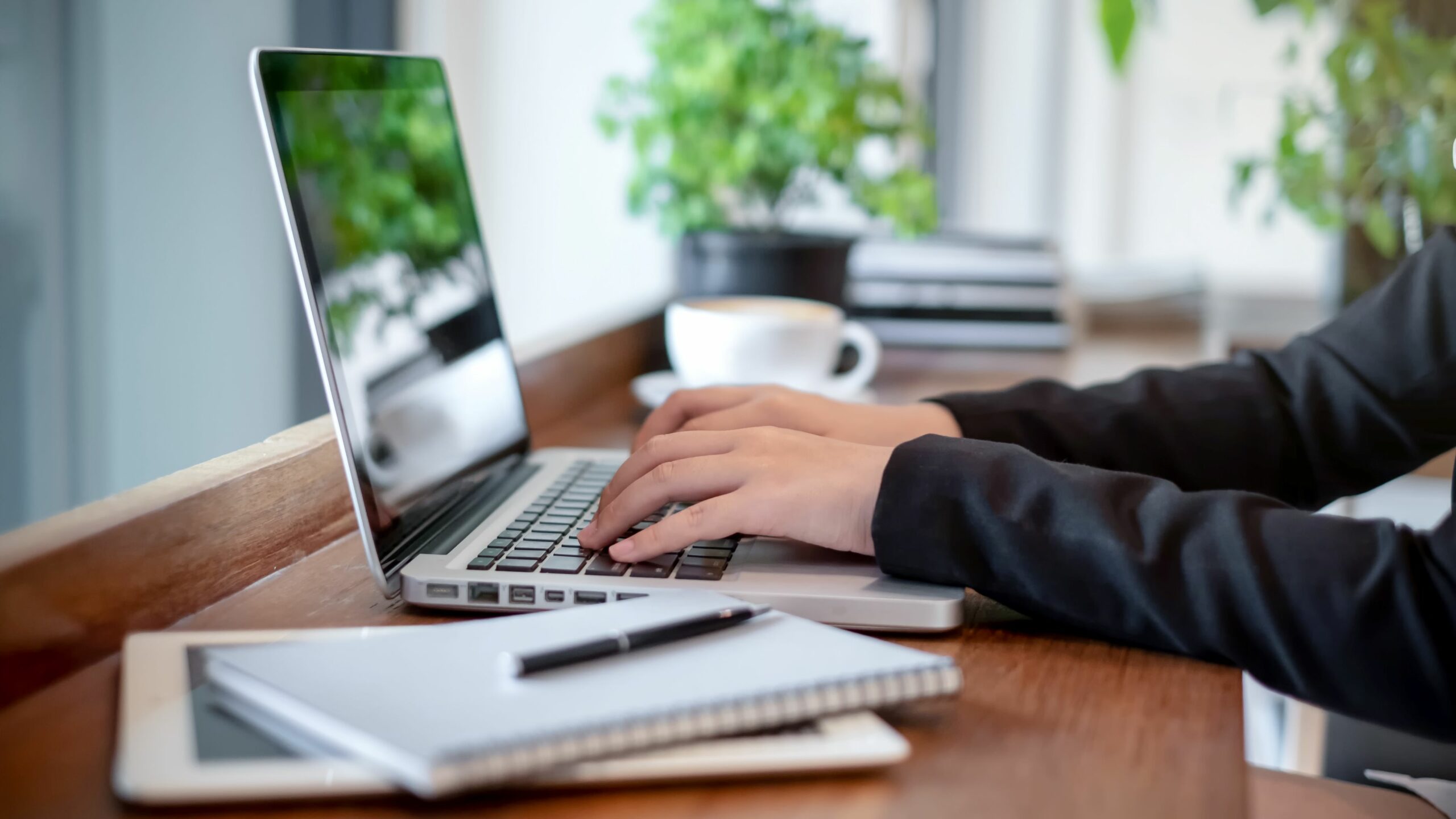 Eine Person arbeitet am Laptop, daneben liegen Notizbuch und Smartphone.
