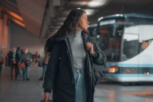 A female traveler with suit case is waiting impatiently at the bus station in the evening. 
