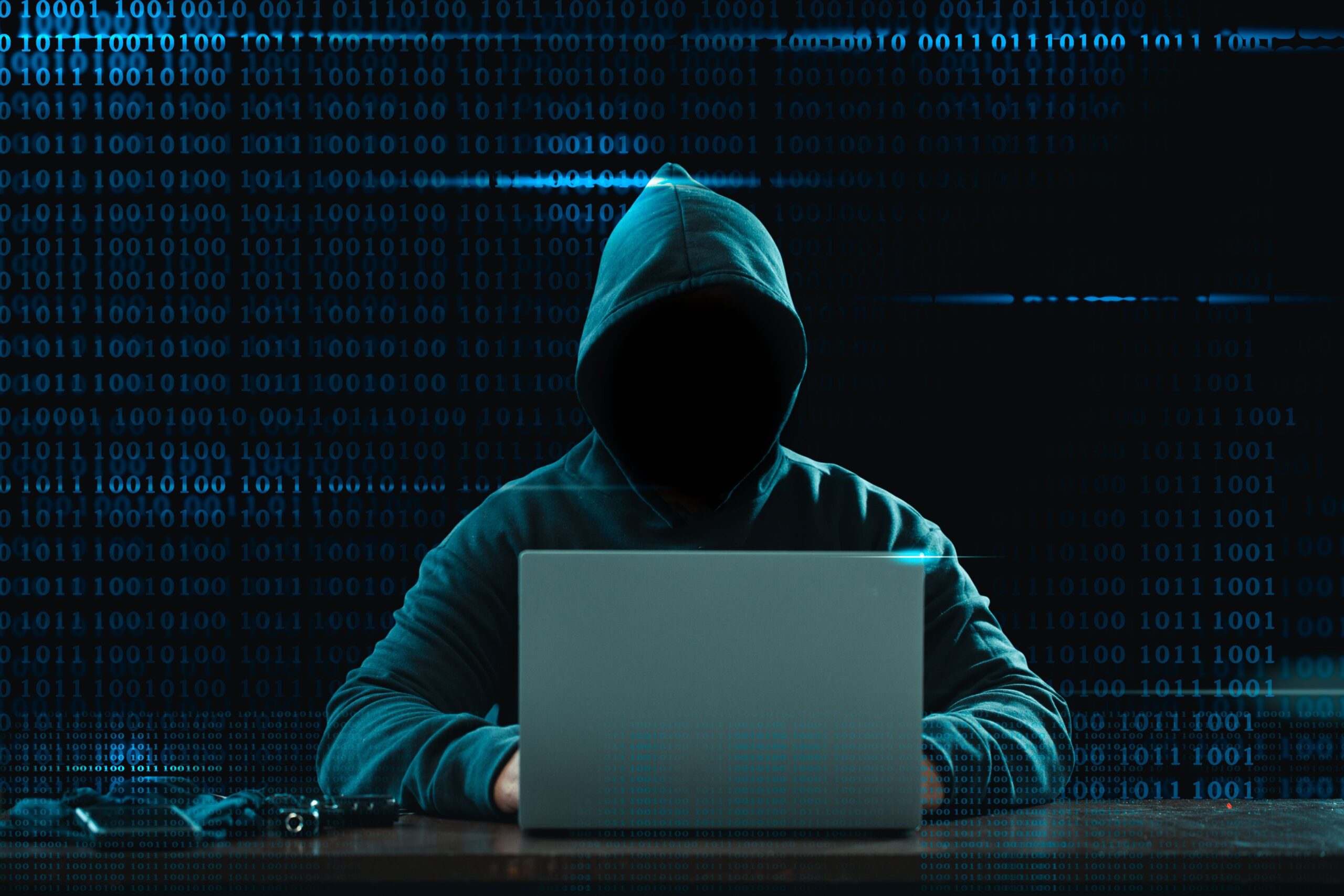 A hacker sits in a dark room in front of his laptop.
