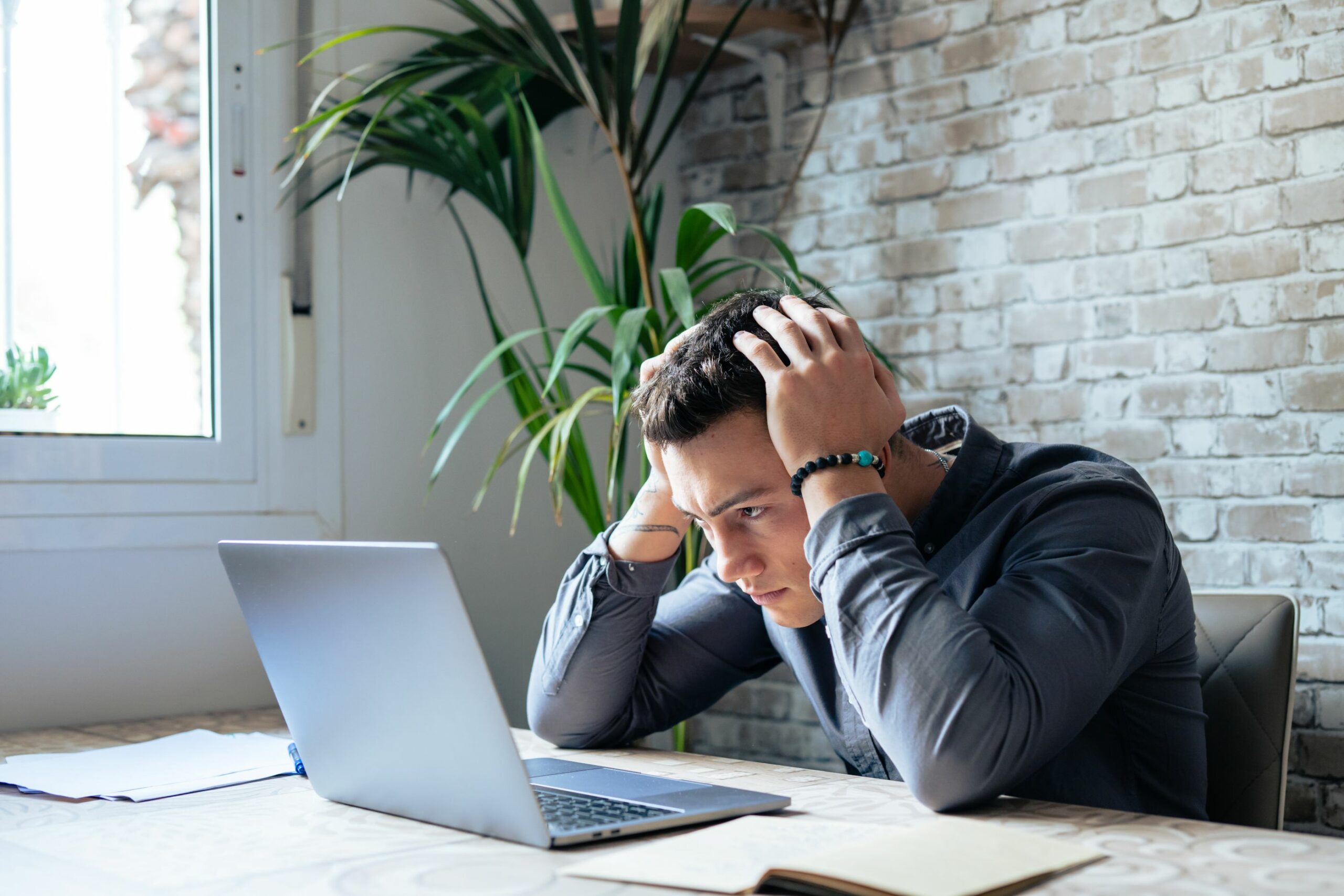 Ein Mann rauft sich die Haare während er auf den Laptop vor sich schaut.