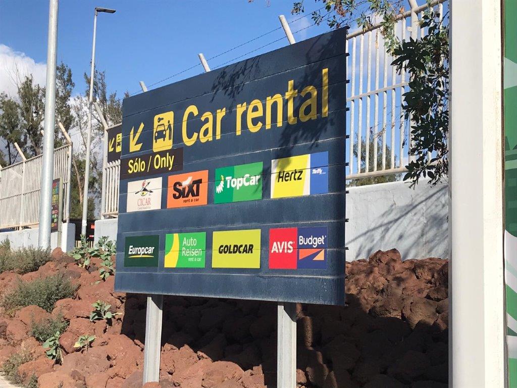 Sign displays logos and names of various car rental companies (Goldcar, Hertz, Sixt, etc.)