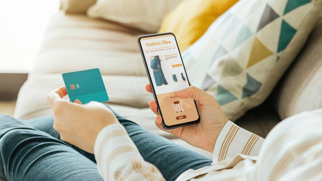 A woman with her smartphone while ordering clothes online. In her other hand she holds her credit card