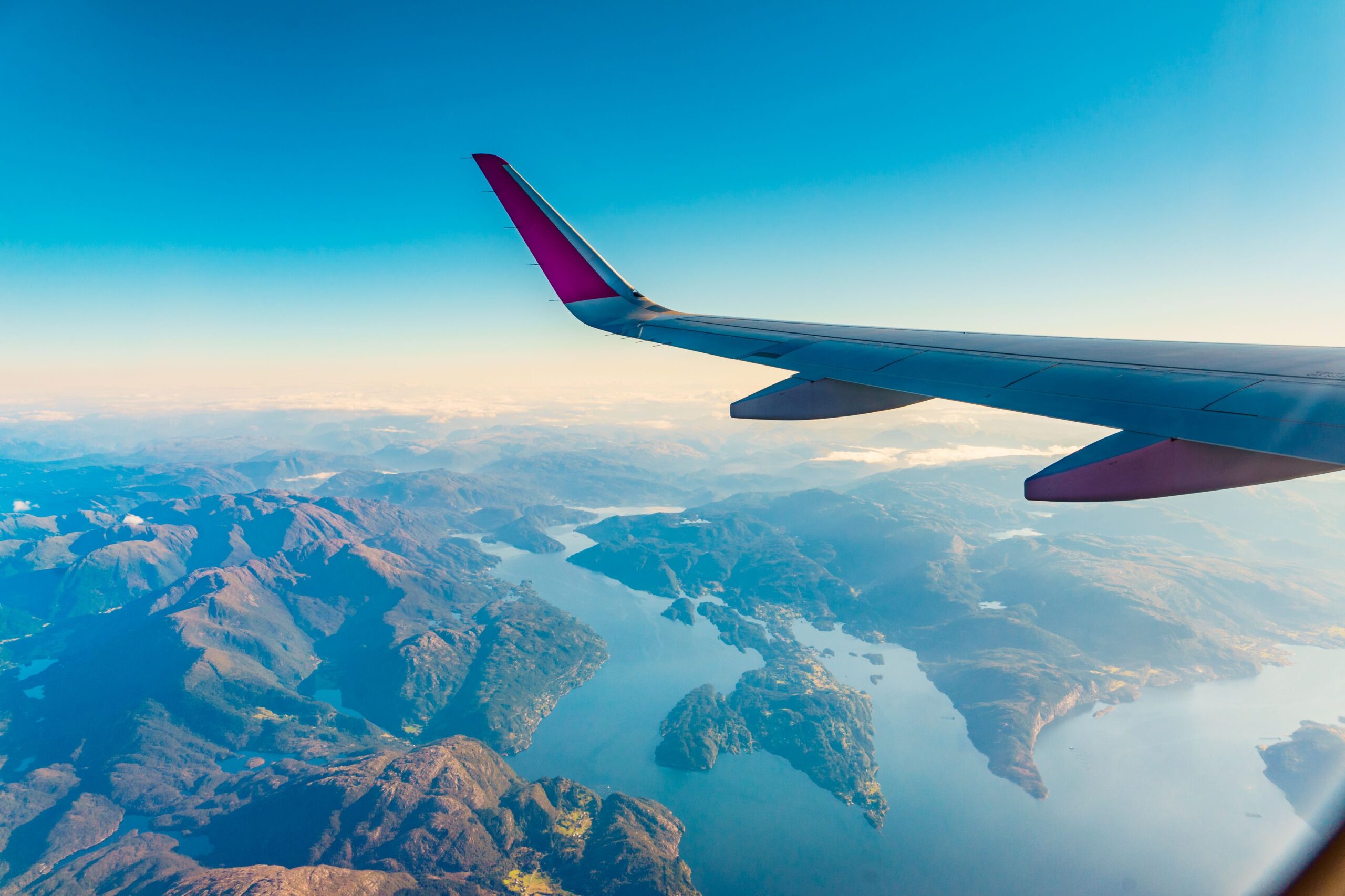 Linke Flugzeugtragfläche mit blauem Himmel und Berge im Hintergrund