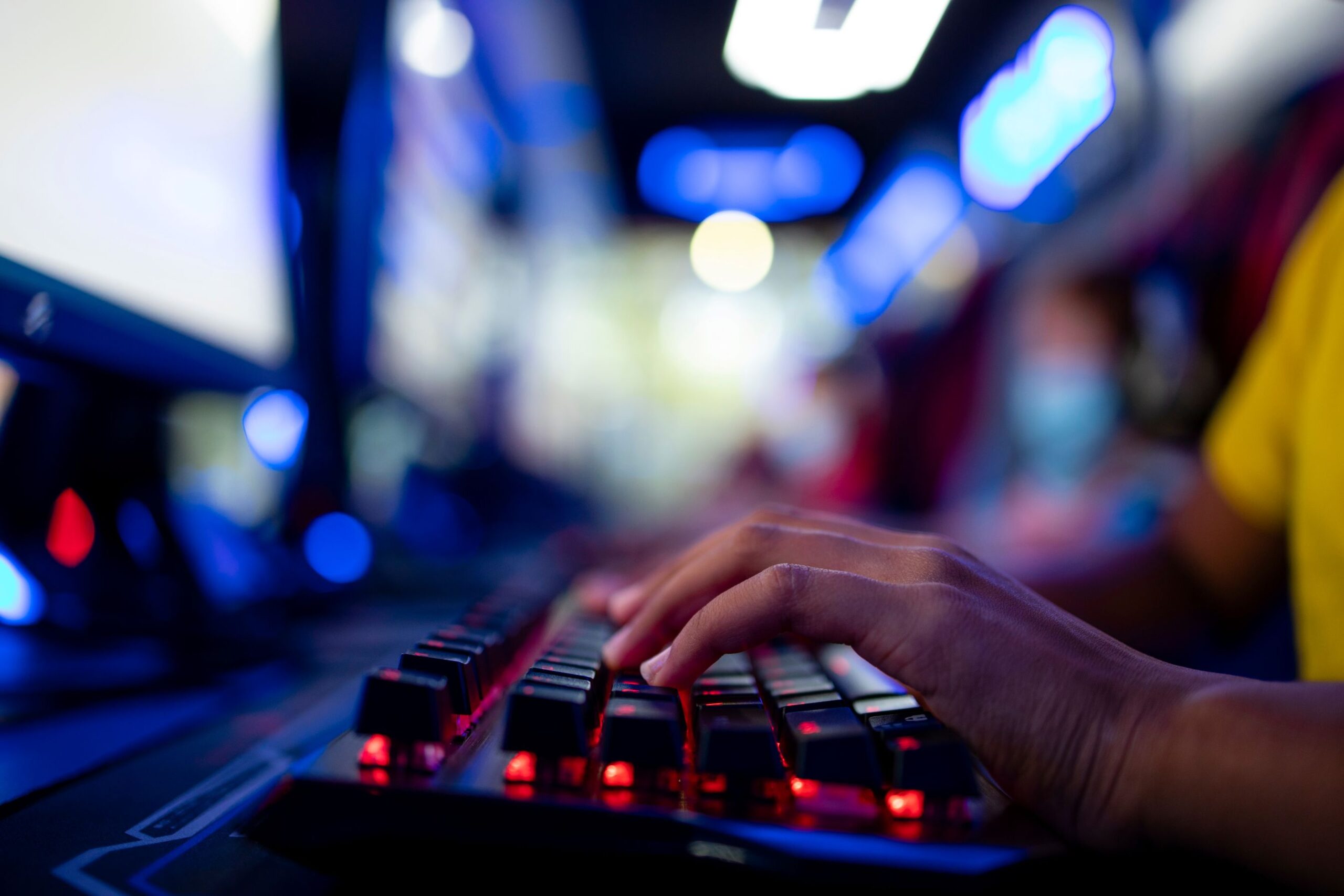 Nahaufnahme einer rot leuchtenden Gaming-Tastatur, eine Person hat die Hände auf den Tasten liegen.