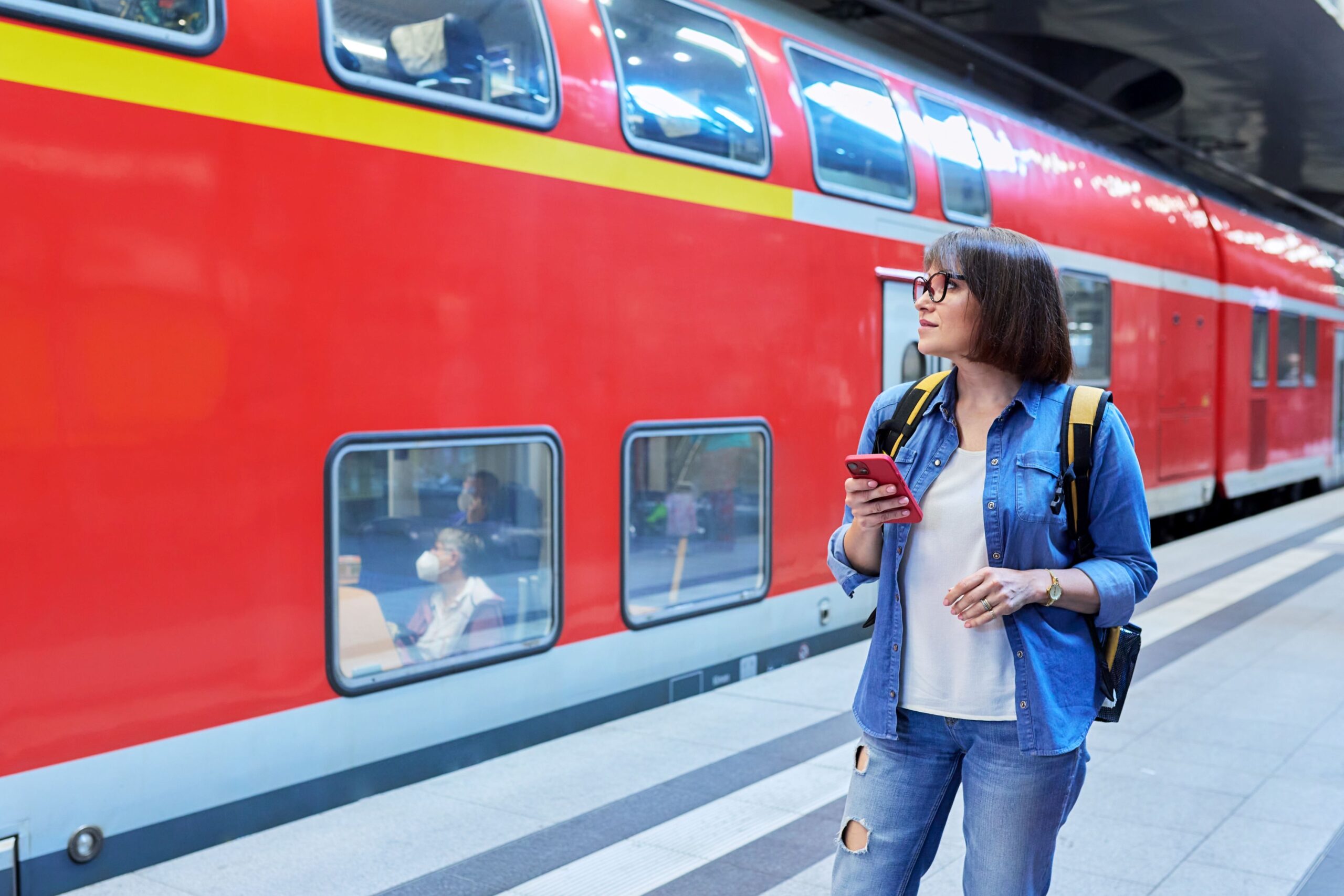 Eine Frau wartet am Bahngleis, im Hintergrund steht eine rote Regionalbahn.