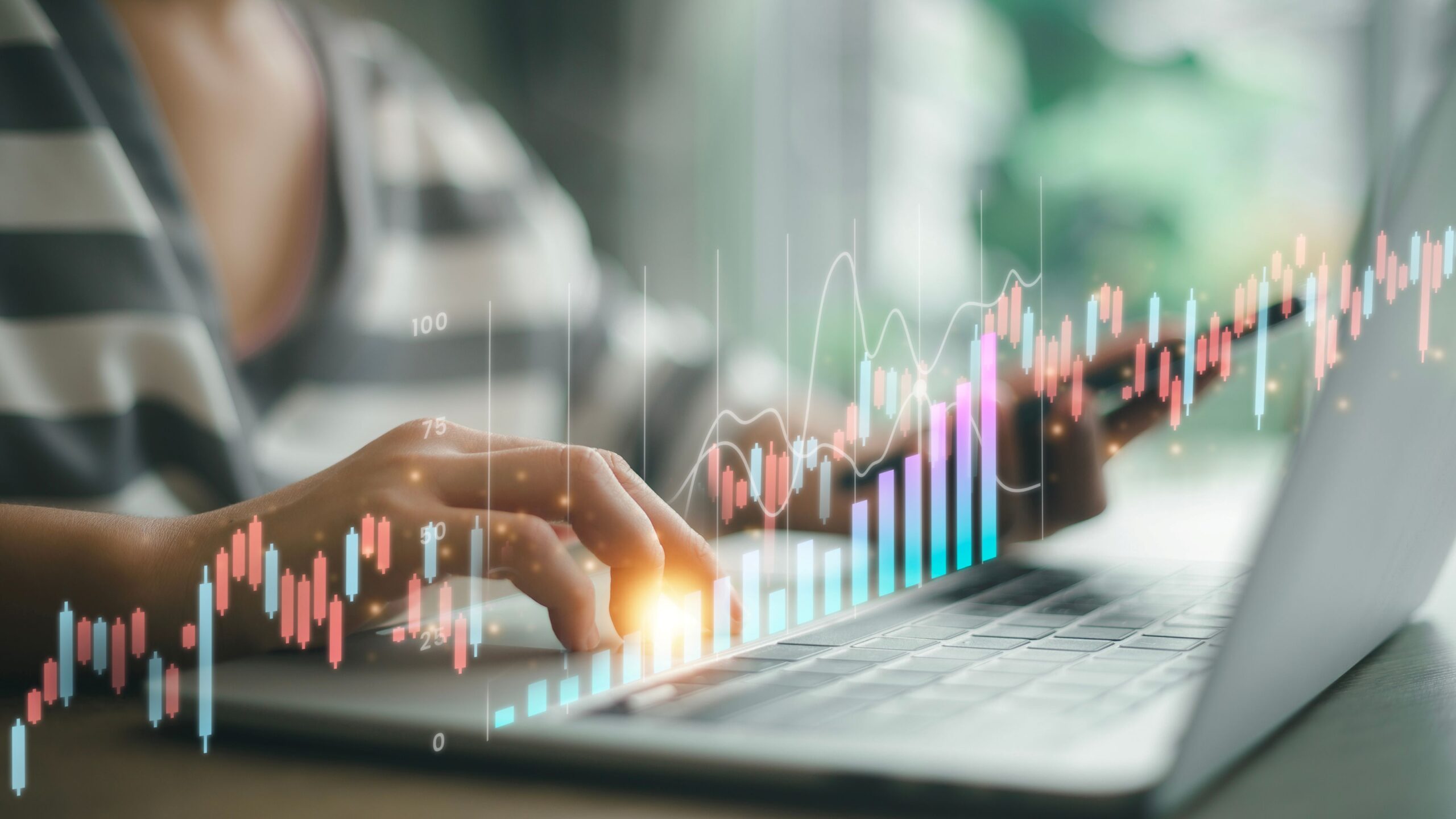 Eine Person arbeitet am Laptop. Im Vodergrund schweben Graphen vom Online-Trading über das Bild