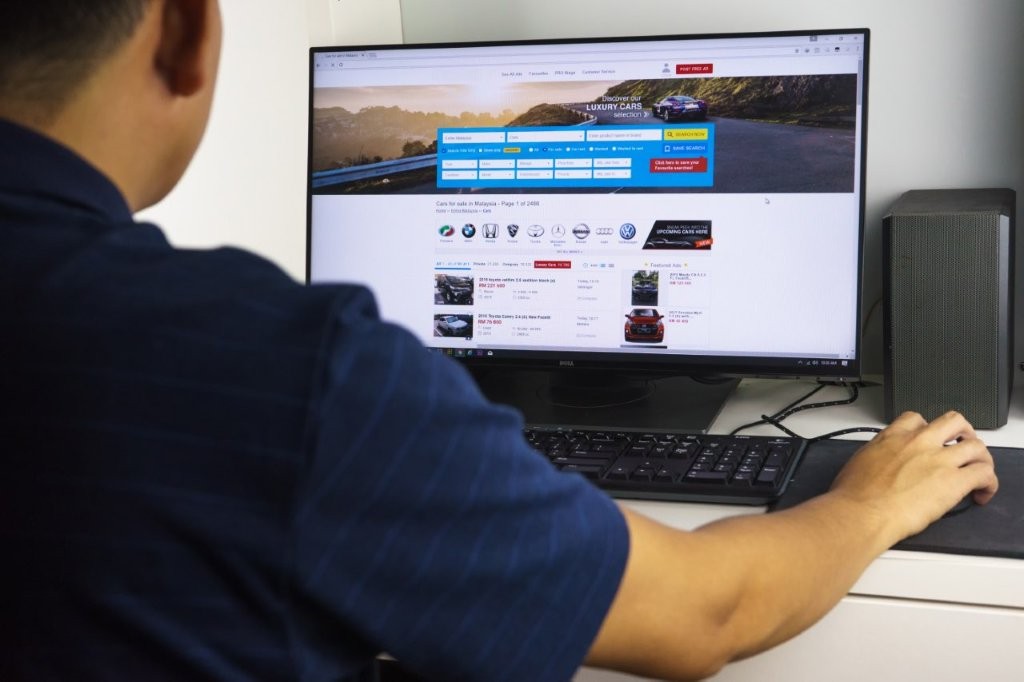 Ein Mann sitzt am Schreibtisch und sucht auf einem Online-Portal ein Auto zum Kauf.
