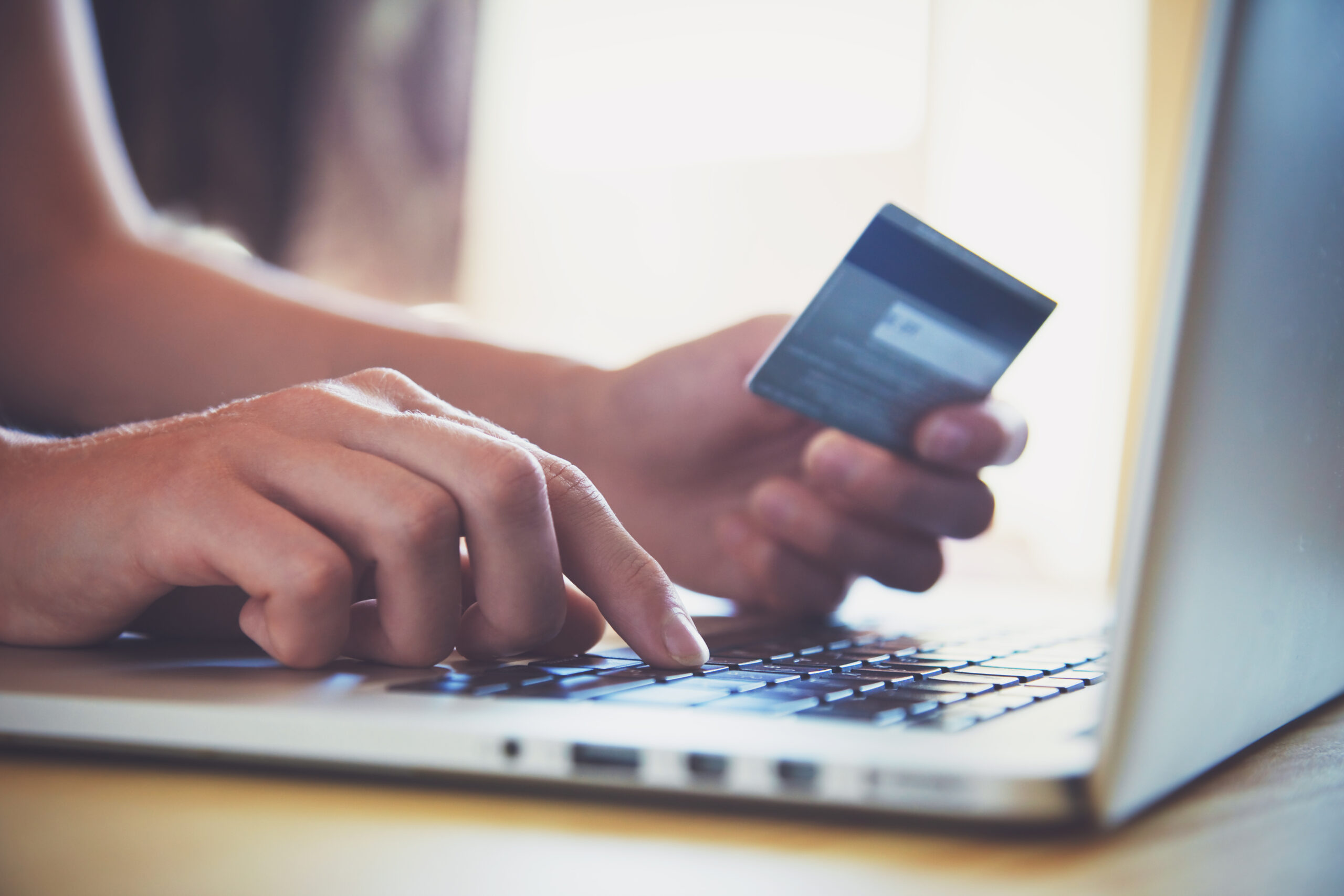 A close-up of a left hand holding a credit card and a right hand typing on a computer