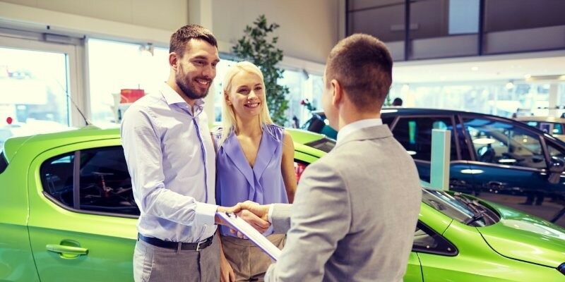 Ein Paar steht mit einem Verkäufer im Autohaus vor einem grünen Auto.