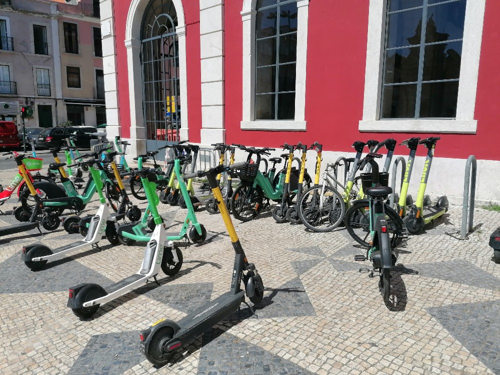 Mehrere E-Roller und Fahrräder zum Ausleihen stehen vor einem Gebäude in der Innenstadt