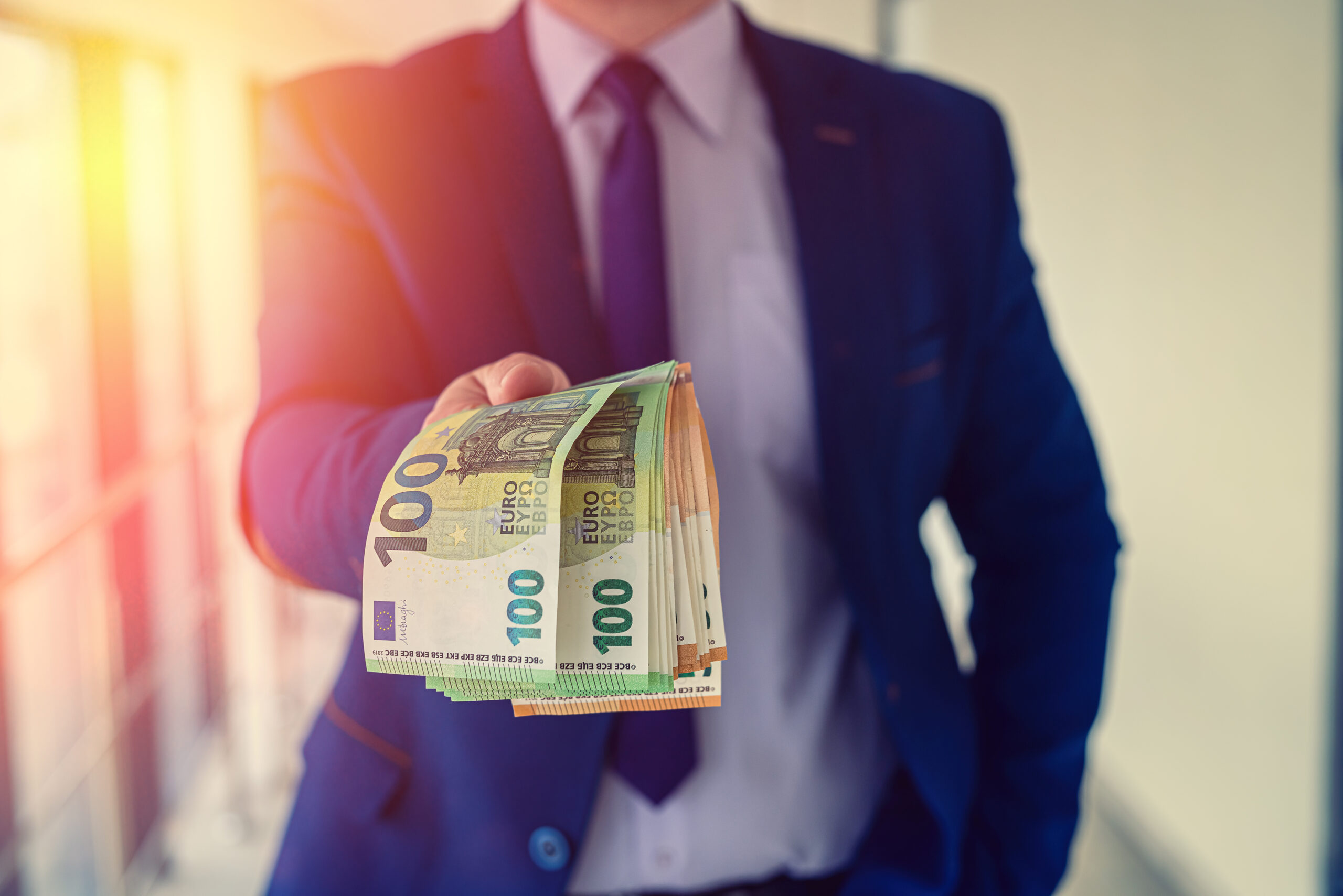 Mann im Anzug hält Euro-Scheine in die Kamera