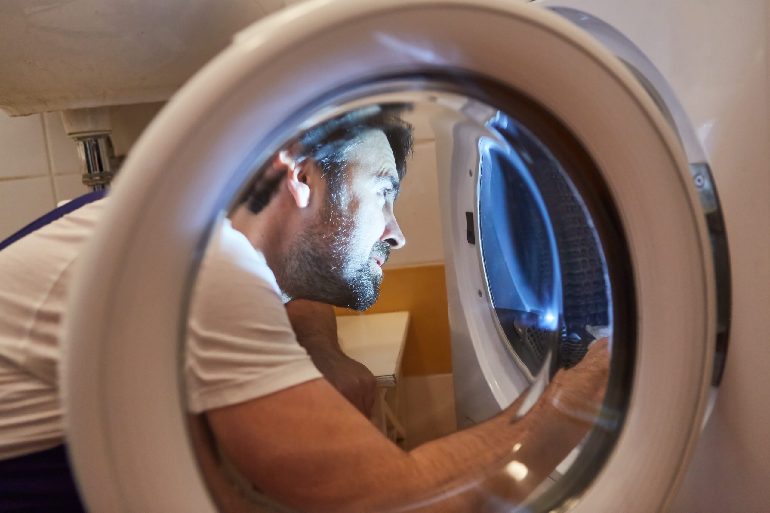 Man is inspecting a washing machine by using a flashlight
