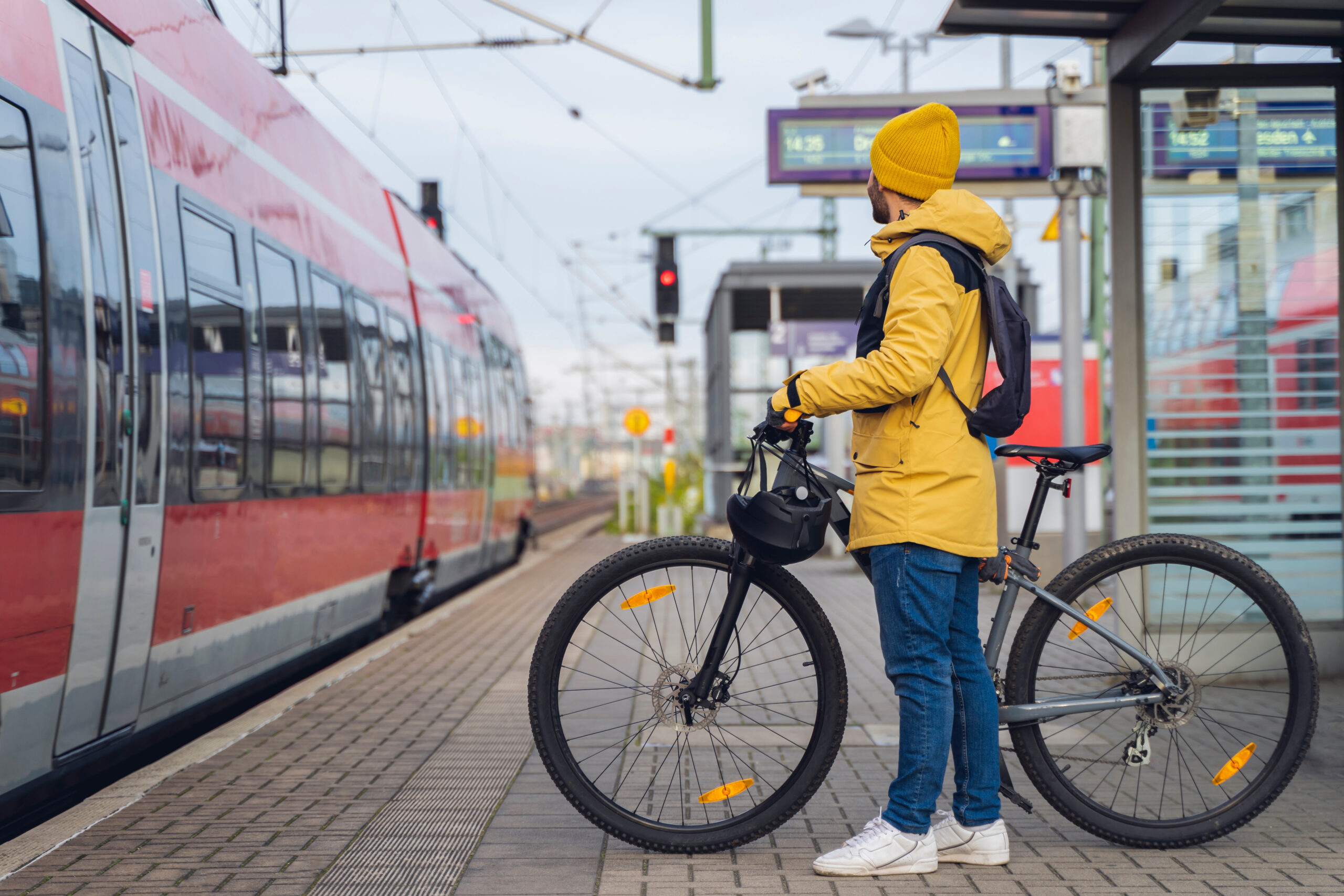 Mann mit gelber Regenjacke und Fahrrad steht am Bahnsteig vor einem roten Zug