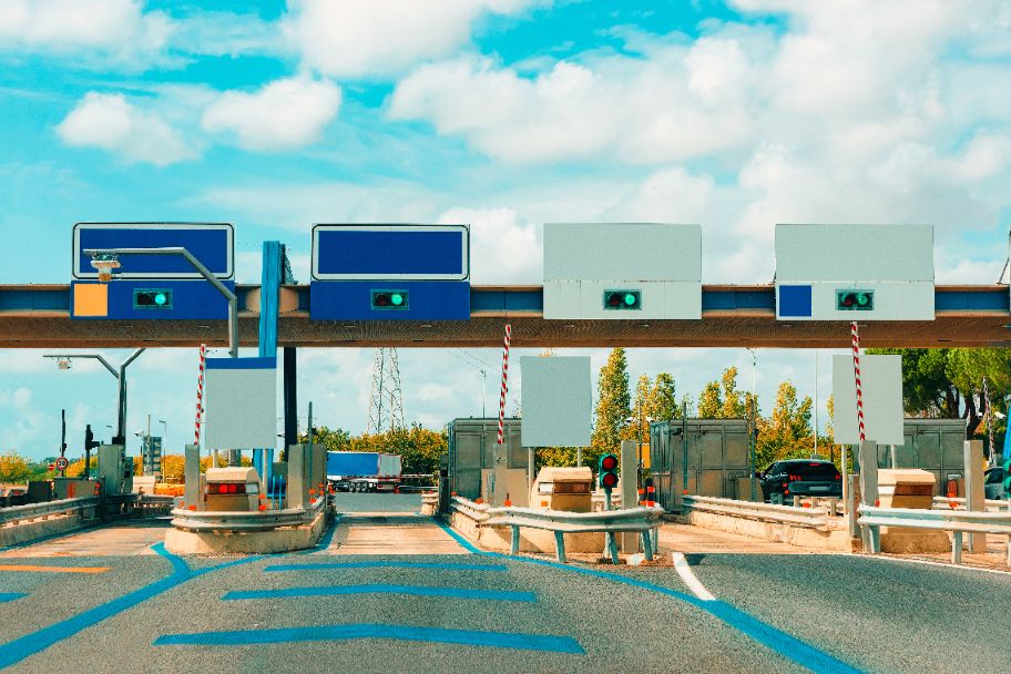 A multi-lane toll booth in Italy with barriers, green traffic lights and cars.