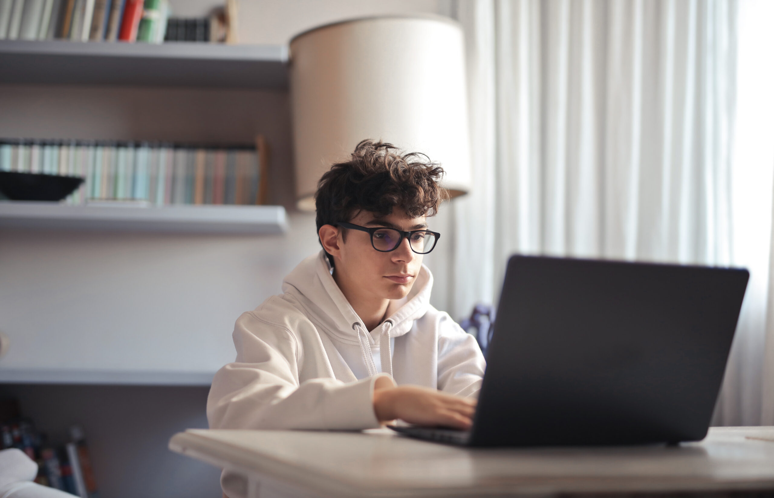 Teenager mit Brille sitzt an einem Laptop