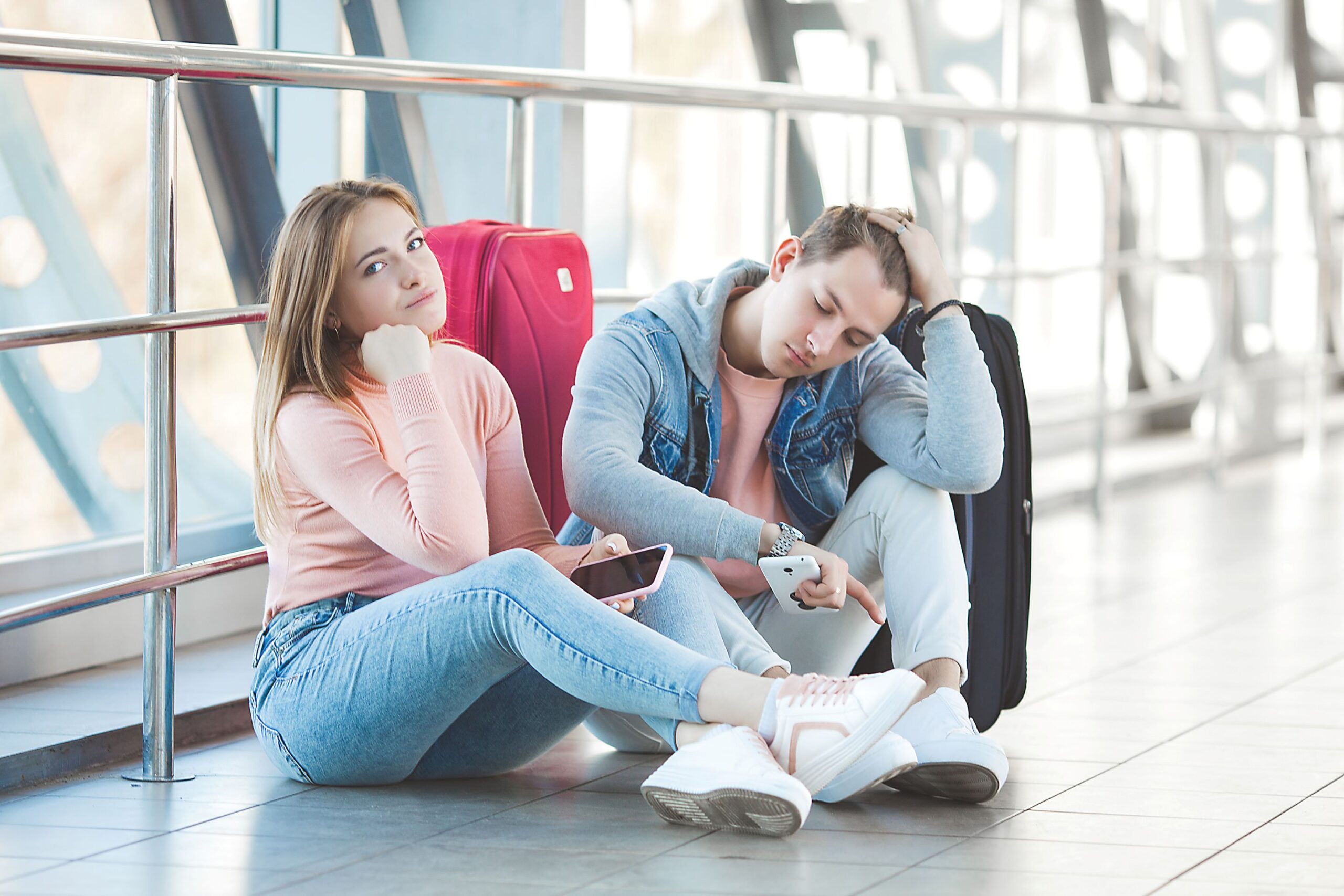 Ein Paar sitzt geknickt auf dem Boden im Wartebereich des Flughafens.
