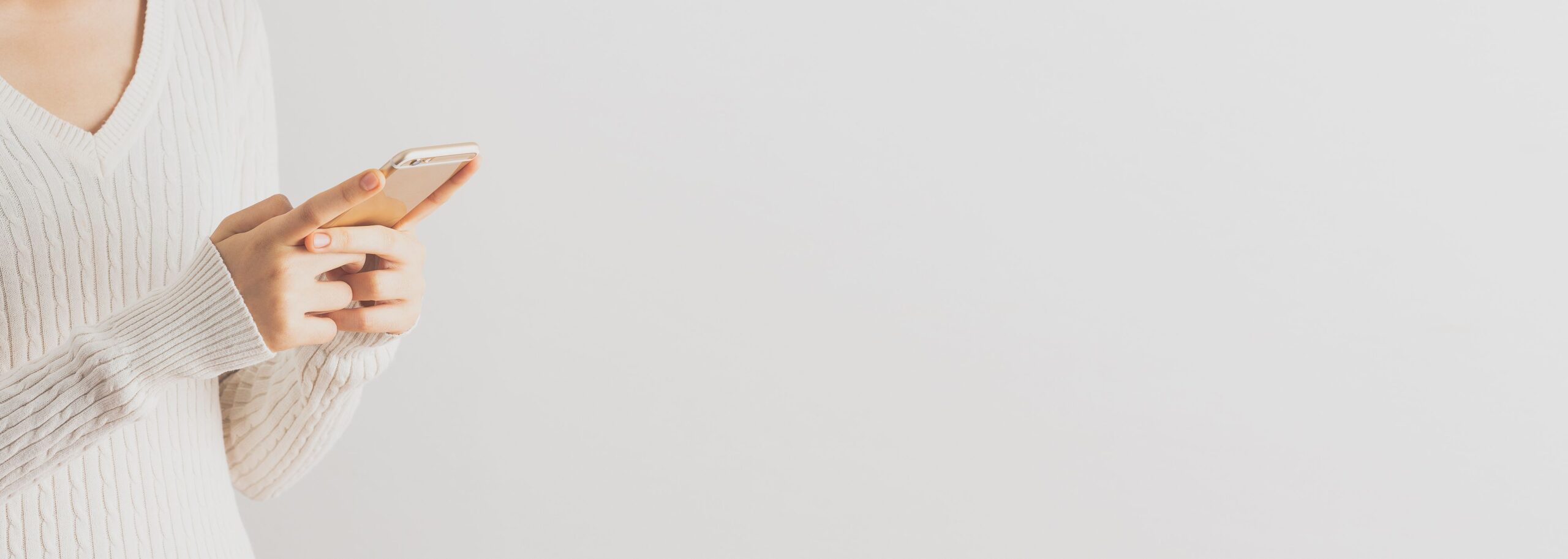 Eine Frau im Wollpullover tippt auf dem Smartphone.