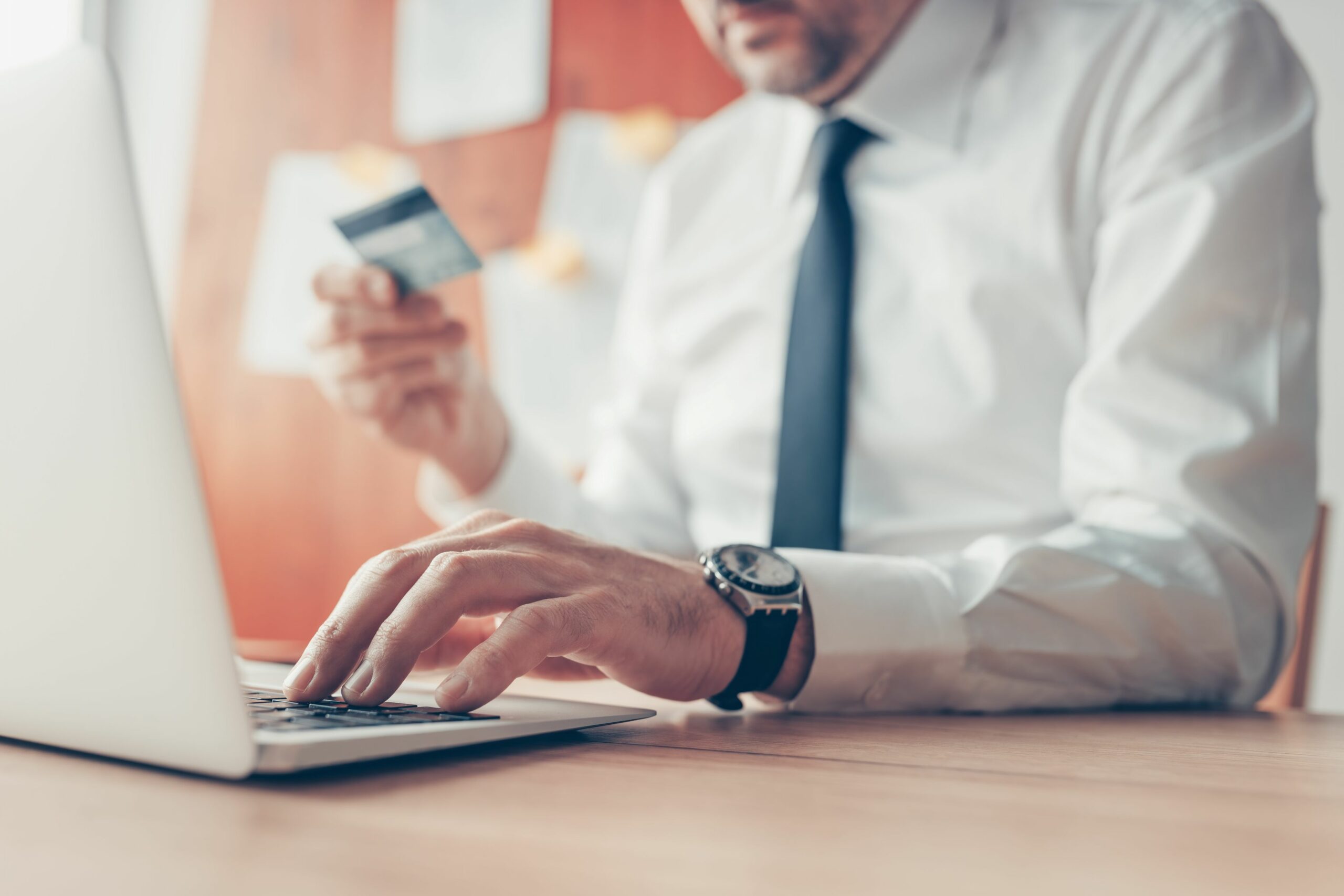 Ein Mann bezahlt etwas über das Online-Banking an seinem Laptop und hält seine Bankkarte dafür in der Hand.