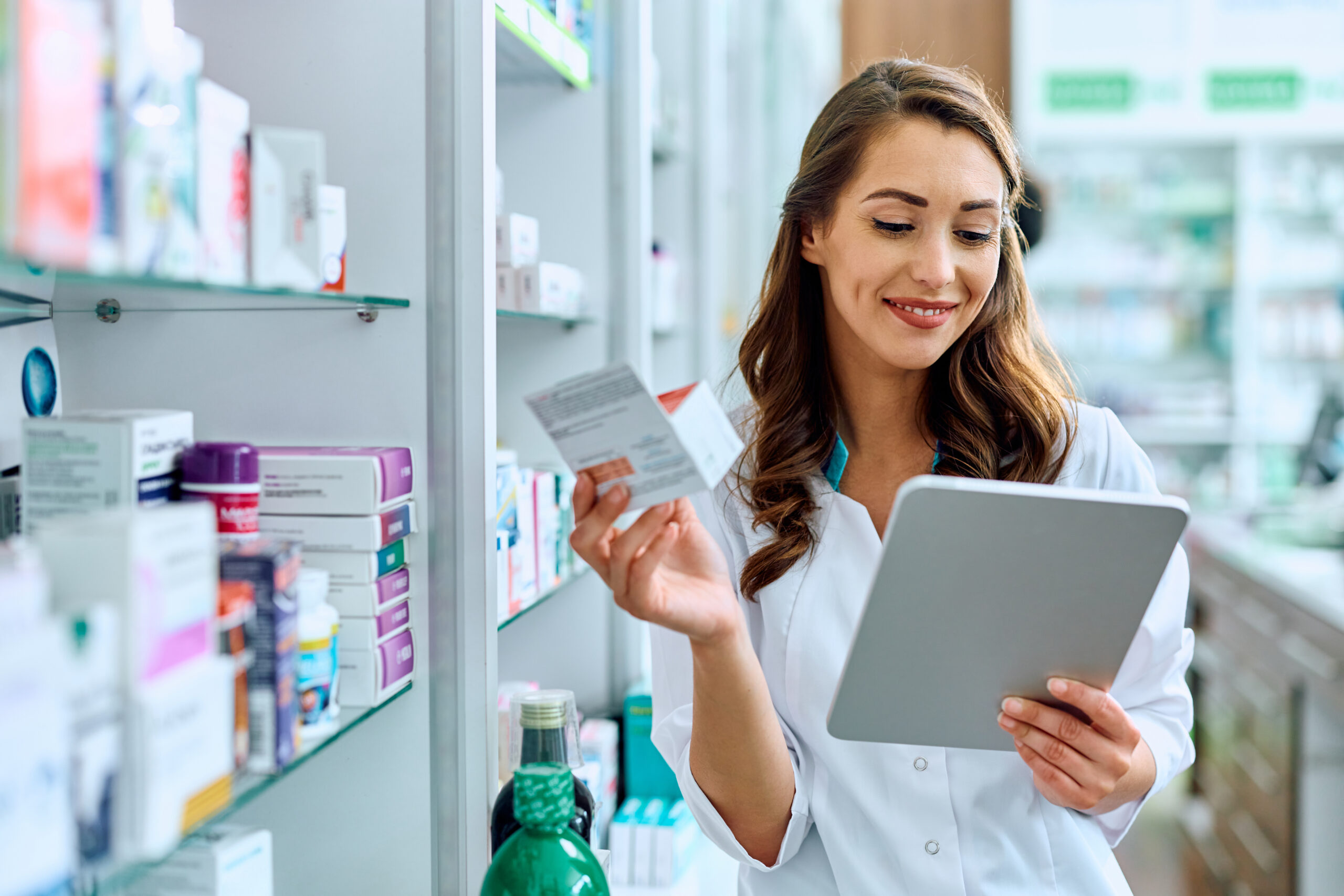 Eine Apothekerin nimmt eine Tablettenpackung aus dem Regal und prüft die Bestellung auf dem Smartphone in ihrer Hand.