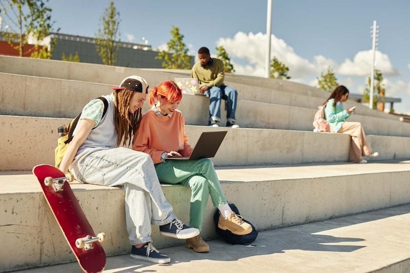 Jugendliche sitzen auf Bänken mit Laptops und Smartphones.
