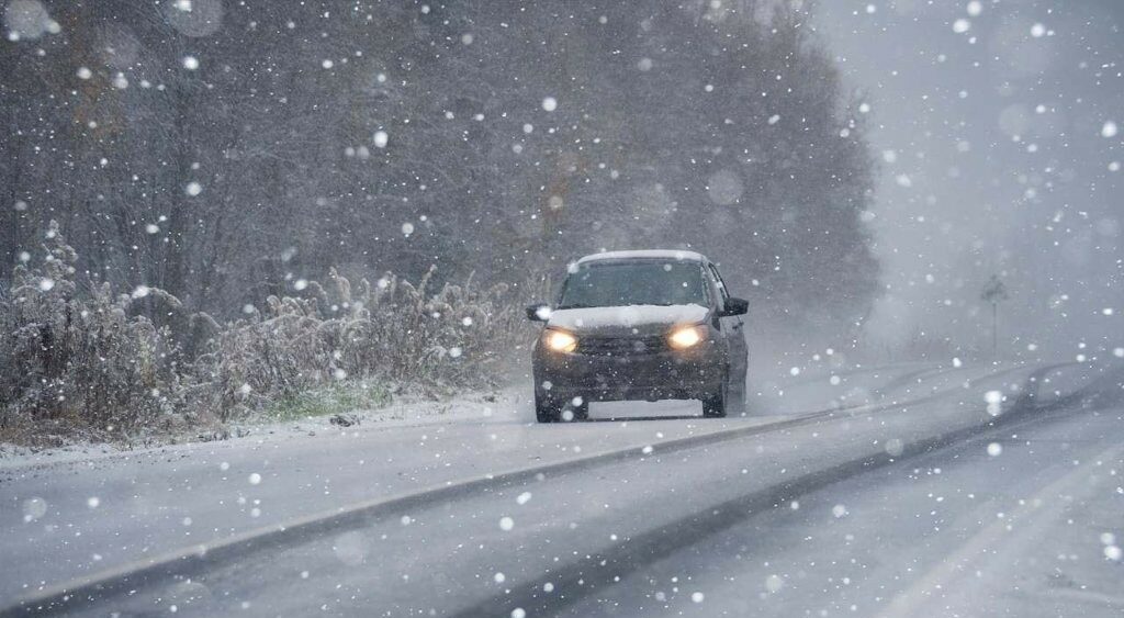 Auto fährt bei Schneefall über eine schneebedeckte Landstraße.