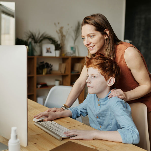Eine Mutter sitzt mit ihrem Sohn vor einem Computer.