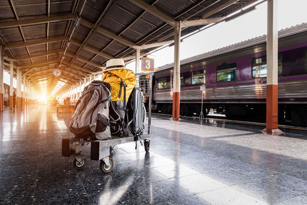 Ein vollbeladener Gepäckwagen mit Koffern steht an einem Bahnsteig. Im Hintergrund steht ein Zug.