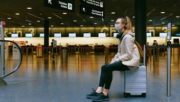 Eine junge Frau sitzt in einem Flughafen-Terminal auf ihrem Koffer.