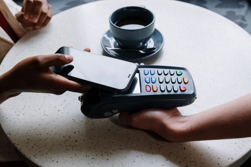 Eine Person bezahlt in einem Café kontaktlos mit dem Smartphone.