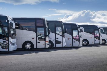 Six white coaches stand in a row in a bus depot.