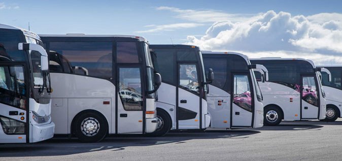 Mehrere weiße Reisebusse stehen in einer Reihe. Reisende profitieren bei Fernbusreisen von den EU-Fahrgastrechten. Mehrere weiße Reisebusse stehen nebeneinander.