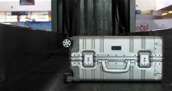Ein silberner Hartschalenkoffer auf einem Gepäckband bei der Sicherheitskontrolle.