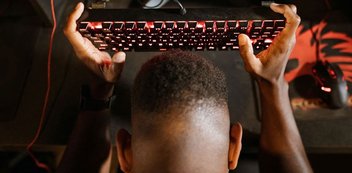 Ein Mann hält sich eine Gaming-Tastatur an den Kopf.