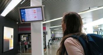 Eine Frau steht in einer Abflughalle und schaut auf einen Monitor mit den aktuellen Abflugzeiten.
