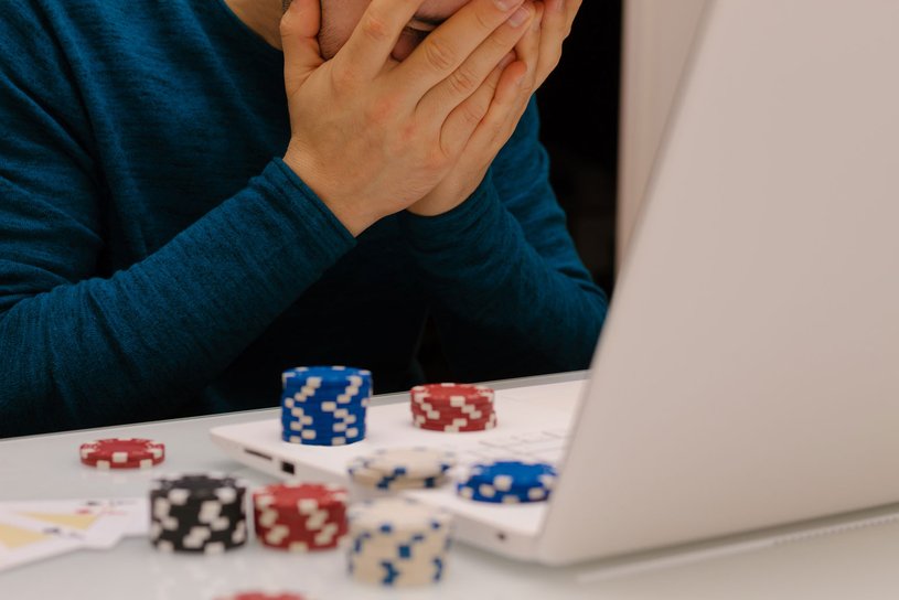 Ein Mann spielt Online-Poker auf seinem Laptop. Er hält sich verzweifelt die Hände vor das Gesicht.