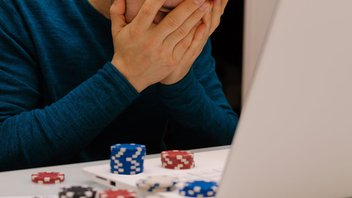 Ein Mann spielt Online-Poker auf seinem Laptop. Er hält sich verzweifelt die Hände vor das Gesicht.