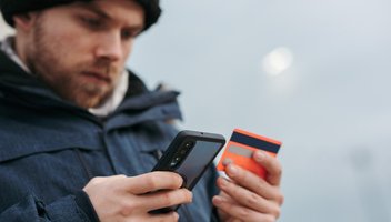 Person hält Kreditkarte und Smartphone in der Hand