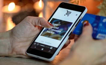 Eine Frau öffnet auf ihrem Smartphone einen Online-Shop. In der rechten Hand hält sie ihre Kreditkarte für die Zahlung bereit.
