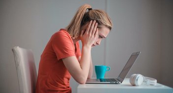 Frau hält sich beide Hände an den Kopf und schaut verzweifelt auf den Bildschirm ihres Computers.