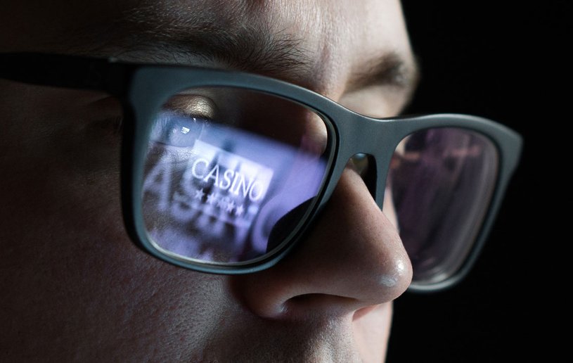 Eine Person mit Brille sitzt vor einem Bildschirm. In der Brille spiegelt sich der Schriftzug: "Casino".