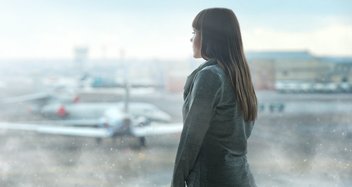 Eine Frau steht in einer Abflughalle und schaut auf Flugzeuge.