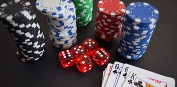 Auf einem Casino-Tisch liegen Würfel, Jetons und Poker-Karten.