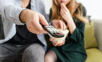 Two people are sitting on a sofa. One of them is holding a remote control.