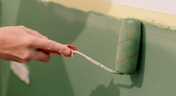 Eine Person hält einen Pinsel in der Hand und streicht eine Wand mit grüner Farbe.