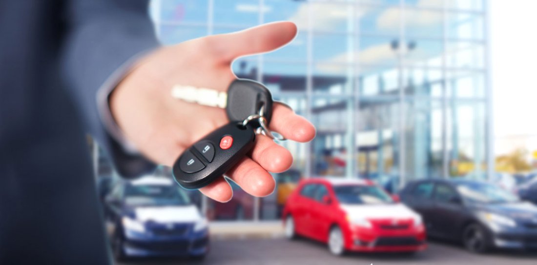 Ein Autoverkäufer hält einen Fahrzeugschlüssel in der Hand. Im Hintergrund stehen Autos.