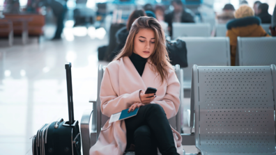 Frau sitzt im Wartebereich eines Flughafens und schaut auf ihr Smartphone