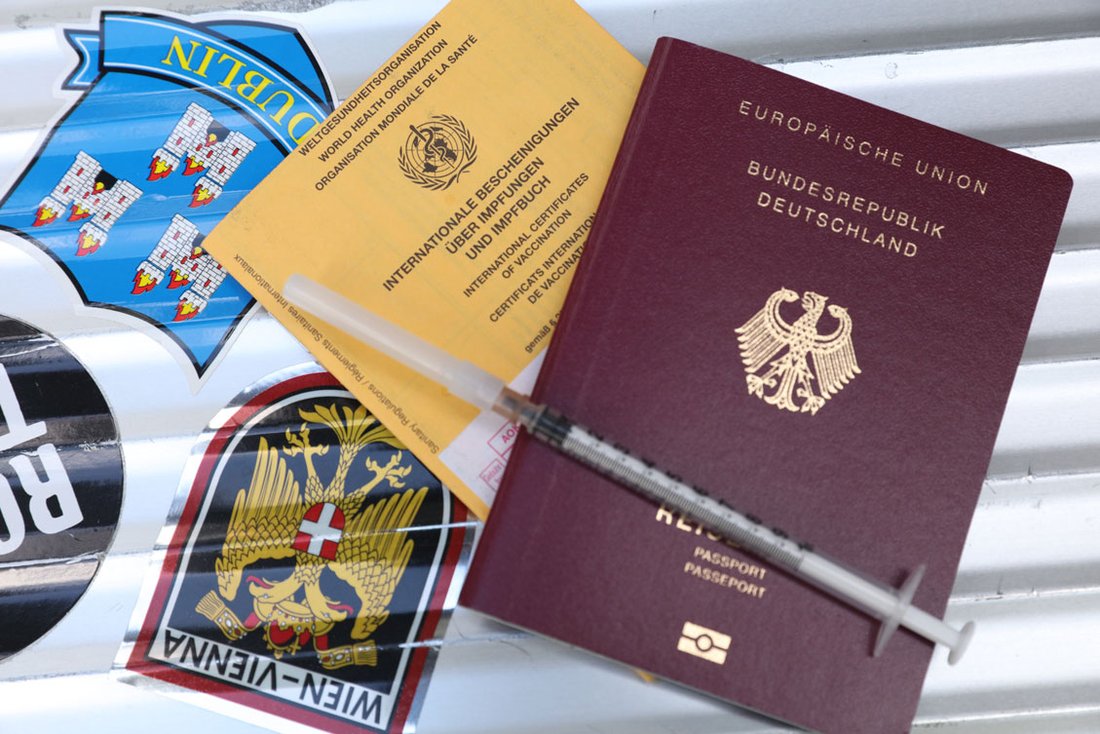 Ein Impfausweis und ein deutscher Reisepass liegen auf einem Gepäckkoffer.