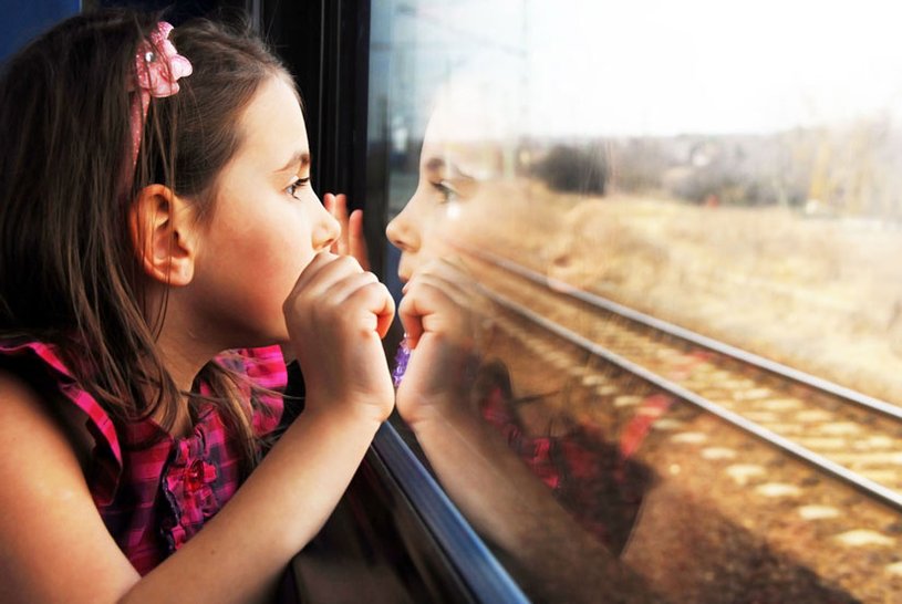 Ein kleines Mädchen sitzt in einem Zugabteil und schaut aus dem Fenster.
